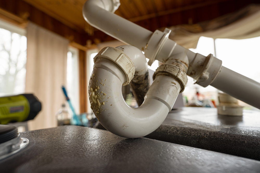 Close-up of a white PVC P-trap plumbing pipe under a sink, showing residue buildup and some dirt on the pipes.