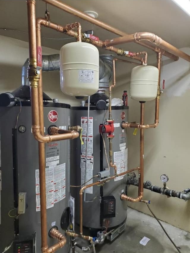 Two water heaters are connected by an intricate system of copper pipes, valves, and expansion tanks in a utility room.
